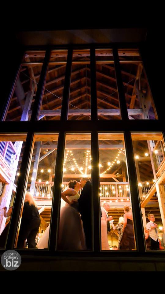 Bride and groom sharing a kiss in front of a big window at night inside Pat's Barn.�