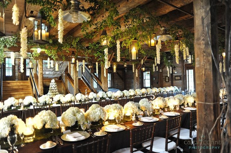 Inside of Pat's Barn showing greenery and lights decorating theceiling over decorated dining tables.�