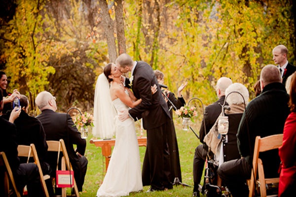 Husband and wife sharing a kiss during their outdoor wedding ceremony.�